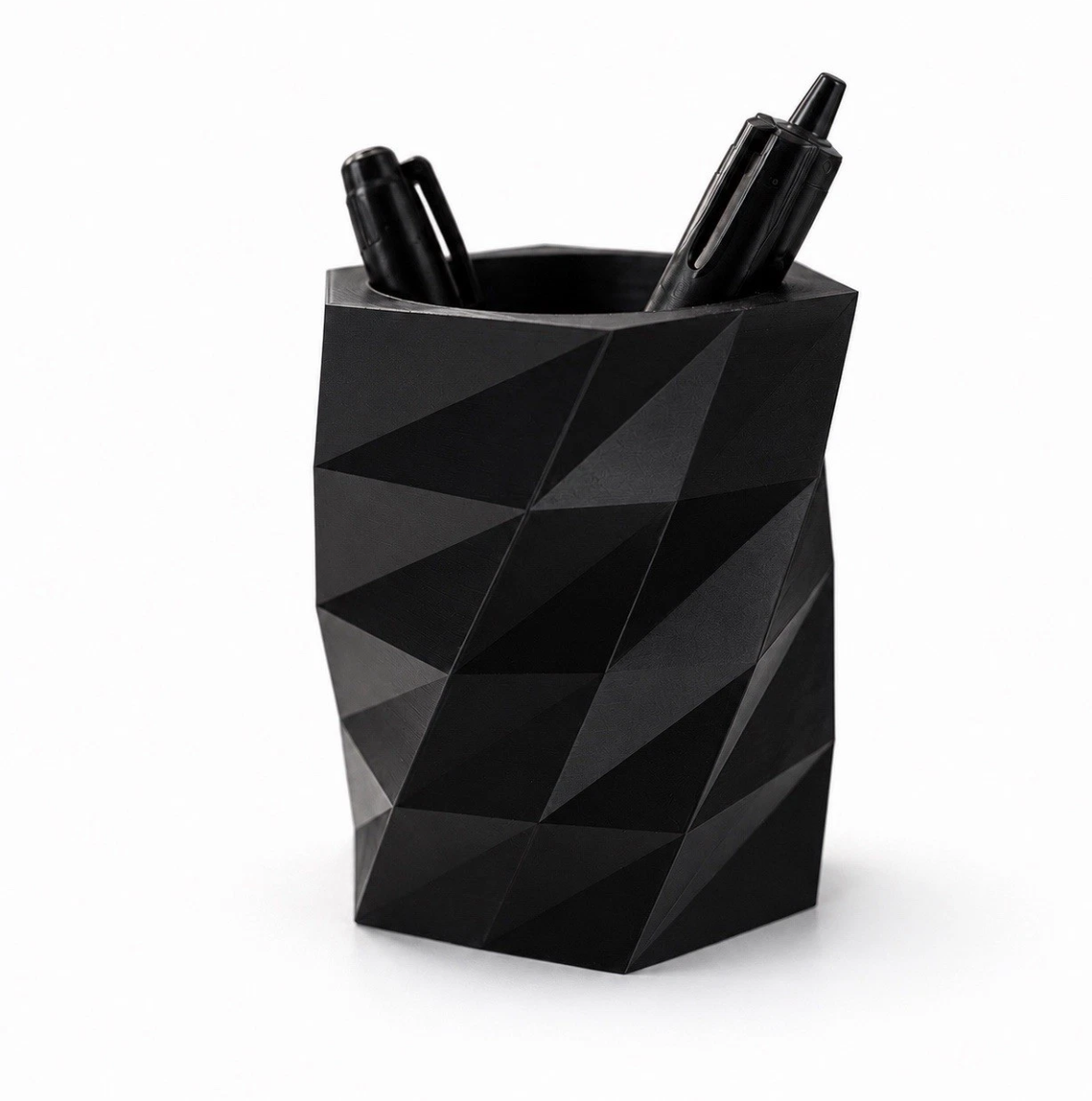 Black geometric pen holder with three pens on a white background